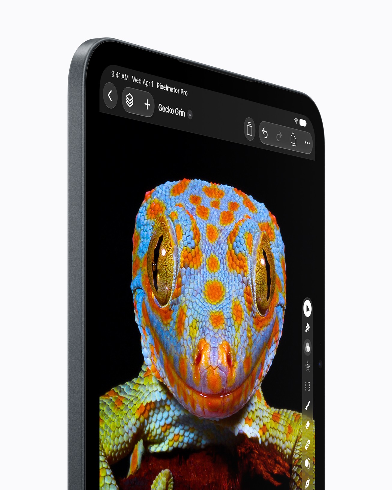 Side view of an iPad mini, its screen showing a close-up of a blue and orange gecko in Pixelmator Pro, with a column of tool icons on the right. Text: the top bar shows the time and date, then “Pixelmator Pro”, with the file name “Gecko Grin” on the line below.
